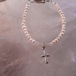 May include: A delicate pearl bracelet with a silver cross charm. The bracelet is made of small, white pearls and has a simple, elegant design.