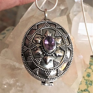 May include: A silver locket necklace with an intricate design and a purple gemstone in the center.