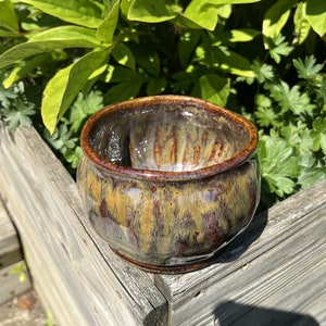 以下が含まれることがあります： 木製の表面に置かれた、テクスチャ加工された釉薬を施した、小さく、茶色と黄色のセラミックボウルです。