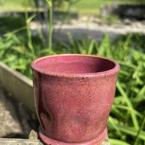 Könnte beinhalten: Eine kleine, gesprenkelte, rotbraune Keramiktasse mit abgerundetem Boden und leicht ausgestelltem Rand.