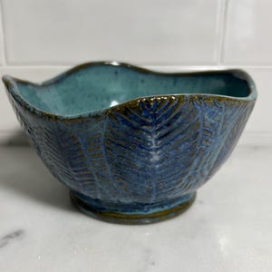 May include: A blue and green ceramic bowl with a wavy rim and a fern leaf design.