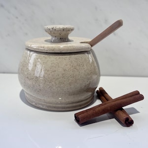 Puede incluir: Una taza de cerámica blanca con un asa negra y el texto "But First, Coffee" en negrita negra. La taza se encuentra sobre un fondo neutro, resaltando su diseño simple.