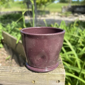 Könnte beinhalten: Eine tiefviolette Keramiktasse mit einem gesprenkelten Überzug. Die Tasse steht auf einer Holzoberfläche.