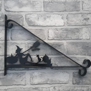 May include: Black metal wall bracket with a silhouette of a witch riding a broomstick with two cats and pumpkins.