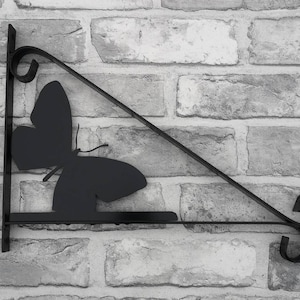 May include: Black metal butterfly wall bracket with a decorative scroll design. The bracket is triangular in shape and has a flat surface for hanging items.