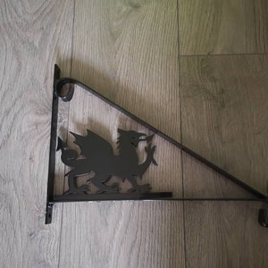 May include: Black metal wall bracket featuring a dragon design. The bracket is triangular in shape with a decorative scroll at the end.