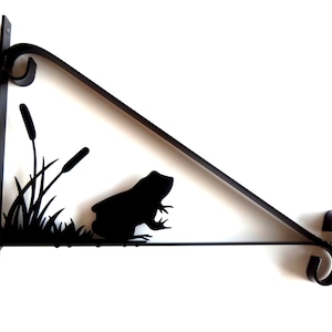 Könnte beinhalten: Schwarze Wandhalterung aus Metall mit einer Silhouette von einem Frosch und Schilf.