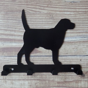 以下が含まれることがあります： 3つのフックが付いた黒い金属製の犬のシルエットのキーフック。犬は尻尾を上げて立っており、シンプルなデザインです。