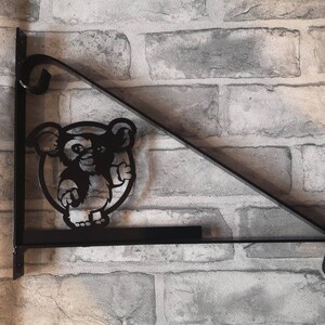May include: Black metal hanging bracket with a decorative silhouette of a cartoon monkey giving a thumbs up. The bracket has a shelf and a decorative scroll design.