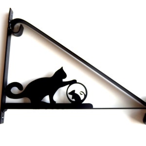 May include: Black metal wall mount bracket with a silhouette of a cat playing with a mouse. The bracket is triangular in shape with a decorative scroll design at the ends.