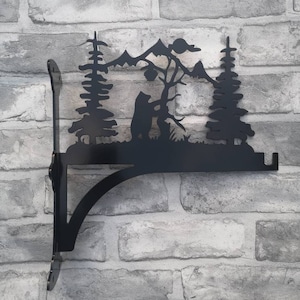 Op de afbeelding: Zwarte metalen plankensteun met een silhouet van een beer in een boslandschap. De steun is gemonteerd op een bakstenen muur.