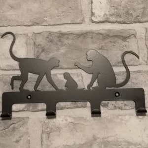 May include: Black metal key holder with three hooks shaped like monkeys. The monkeys are in a family group with a mother, father, and baby monkey.