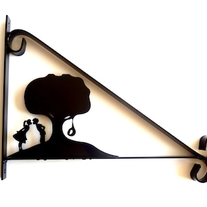 May include: Black metal wall bracket featuring a silhouette of two people kissing under a tree with a swing.
