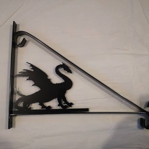 May include: Black metal wall bracket featuring a dragon silhouette design. The bracket is triangular in shape with a decorative scroll at each end.