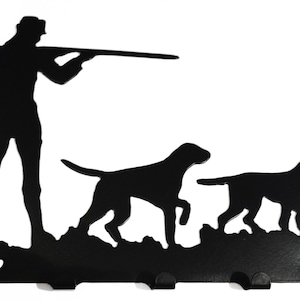 Könnte beinhalten: Schwarzer Schlüsselhalter aus Metall mit einer Silhouette eines Jägers mit zwei Hunden. Der Jäger hält ein Gewehr und die Hunde rennen. Am unteren Ende des Halters befinden sich fünf Haken.