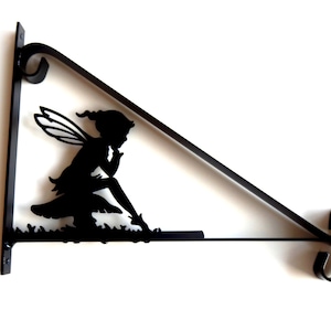 May include: Black metal fairy silhouette wall bracket. The fairy is sitting with her wings spread and her hand on her chin. The bracket is triangular shaped with a decorative scroll at the end.