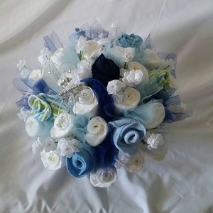 K&ouml;nnte beinhalten: Ein Strau&szlig; handgefertigter Blumen in Blau- und Wei&szlig;t&ouml;nen, mit Akzenten in Marineblau und Hellgr&uuml;n. Die Blumen sind kreisf&ouml;rmig angeordnet und mit durchsichtigem blauem Band und kleinen wei&szlig;en Bl&uuml;ten verziert.