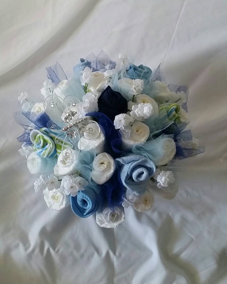 K&ouml;nnte beinhalten: Ein Strau&szlig; handgefertigter Blumen in Blau- und Wei&szlig;t&ouml;nen, mit Akzenten in Marineblau und Hellgr&uuml;n. Die Blumen sind kreisf&ouml;rmig angeordnet und mit durchsichtigem blauem Band und kleinen wei&szlig;en Bl&uuml;ten verziert.