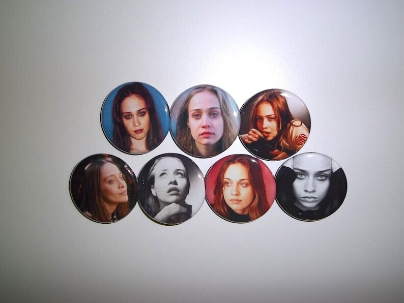 Peut inclure: Un ensemble de sept boutons ronds pr&eacute;sentant des portraits d'une femme. Les boutons affichent diverses images en couleur et en noir et blanc, avec diff&eacute;rentes expressions et poses. Les boutons sont dispos&eacute;s sur une surface blanche.