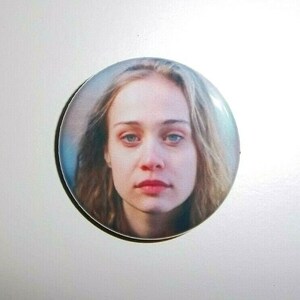 Peut inclure: Un bouton rond repr&eacute;sentant le portrait d'une femme &agrave; la peau claire, aux yeux bleus et aux cheveux ch&acirc;tain clair. L'image est un gros plan du visage de la femme, avec une expression neutre. Le bouton a une finition brillante et un bord noir.