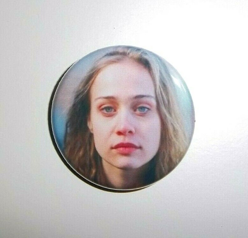 Peut inclure: Un bouton rond repr&eacute;sentant le portrait d'une femme &agrave; la peau claire, aux yeux bleus et aux cheveux ch&acirc;tain clair. L'image est un gros plan du visage de la femme, avec une expression neutre. Le bouton a une finition brillante et un bord noir.