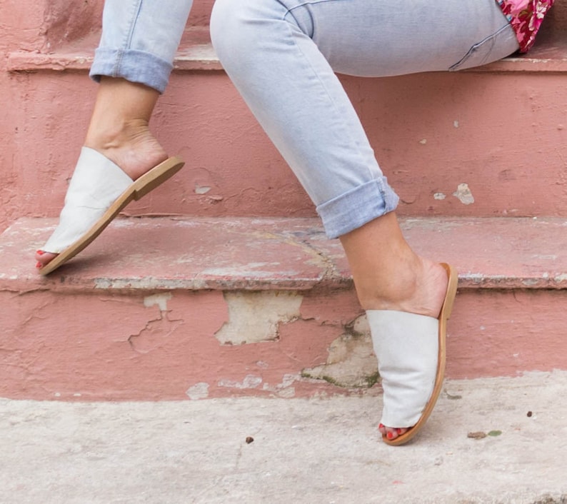 May include: A pair of white leather sandals with a brown sole. The sandals are worn by a person sitting on a set of pink stairs.