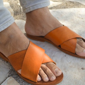 May include: A pair of orange leather sandals with a criss-cross strap design. The sandals have a simple, minimalist style and are perfect for warm weather.