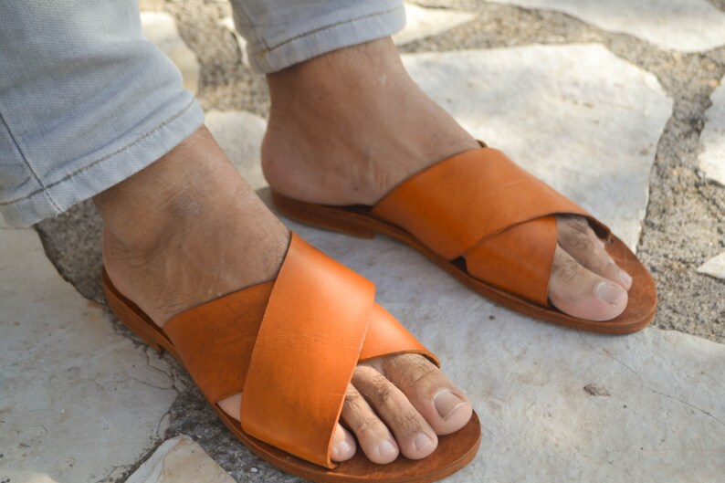 May include: A pair of orange leather sandals with a criss-cross strap design. The sandals have a simple, minimalist style and are perfect for warm weather.