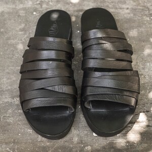 Puede incluir: Un par de sandalias de cuero negro con m&uacute;ltiples correas. Las sandalias tienen un dise&ntilde;o simple y son de dedos abiertos.
