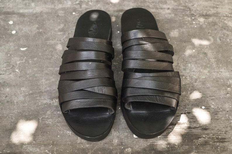 Puede incluir: Un par de sandalias de cuero negro con m&uacute;ltiples correas. Las sandalias tienen un dise&ntilde;o simple y son de dedos abiertos.