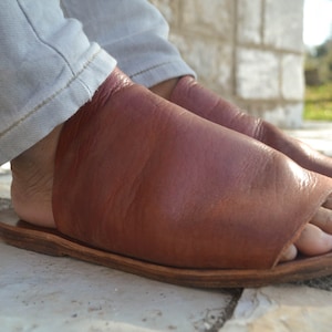 Puede incluir: Un par de sandalias de cuero marr&oacute;n con un dise&ntilde;o de dedo abierto. Las sandalias tienen un estilo simple y minimalista y est&aacute;n hechas de cuero de alta calidad.