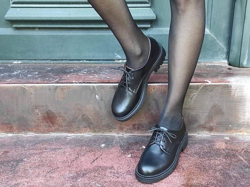May include: Black leather lace-up shoes with a chunky sole. The shoes are worn by a person with black tights.