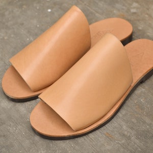 May include: A pair of tan leather sandals with a simple design. The sandals have a flat sole and an open toe.