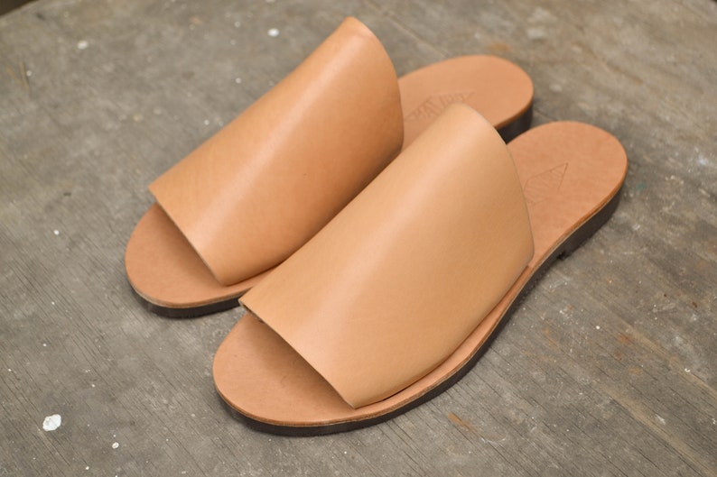 May include: A pair of tan leather sandals with a simple design. The sandals have a flat sole and an open toe.