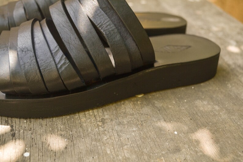 Puede incluir: Sandalias de cuero negro con una suela de plataforma gruesa y m&uacute;ltiples correas a trav&eacute;s del pie.