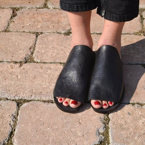May include: A pair of black leather open-toe sandals with a simple design. The sandals have a flat sole and are made of a soft, supple leather.
