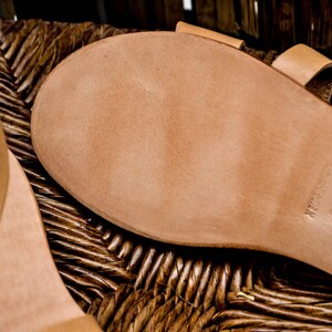 Puede incluir: Primer plano de la suela de una sandalia de cuero marr&oacute;n. La suela est&aacute; hecha de cuero grueso y duradero y tiene una superficie texturizada. La sandalia est&aacute; marcada con el texto "Handmade in Greece".