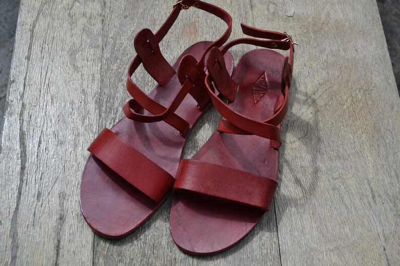 May include: A pair of red leather sandals with multiple straps and buckles. The sandals have a simple design and are made of high-quality leather.