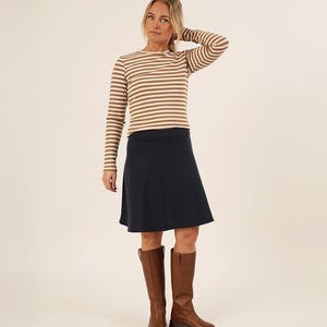 May include: A woman in a brown and white striped top, a navy blue skirt, and brown knee-high boots. The boots have a flat sole. The outfit is casual and suitable for autumn or winter wear.