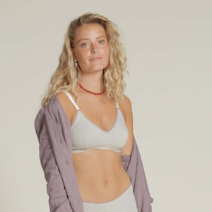 Könnte beinhalten: Ein gestreiftes BH- und Unterwäsche-Set in Grau und Weiß. Der BH hat einen V-Ausschnitt und weiße Träger. Die passende Unterwäsche ist hoch tailliert. Ein langes, hellviolettes Hemd wird offen über dem Set getragen.