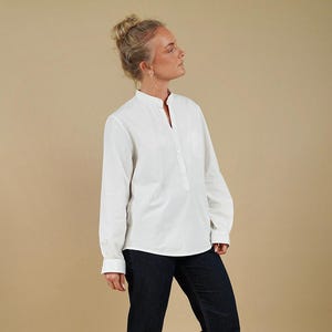 May include: A long-sleeved white shirt featuring a mandarin collar, a partial button-down placket, and a single chest pocket, paired with dark blue denim jeans. The shirt has cuffed sleeves and a straight hemline, while the jeans are full-length.