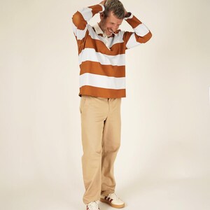 May include: A rugby shirt with horizontal brown and white stripes, paired with khaki pants and white sneakers with burgundy accents. The shirt has a white collar and buttoned placket. The outfit is casual and comfortable.