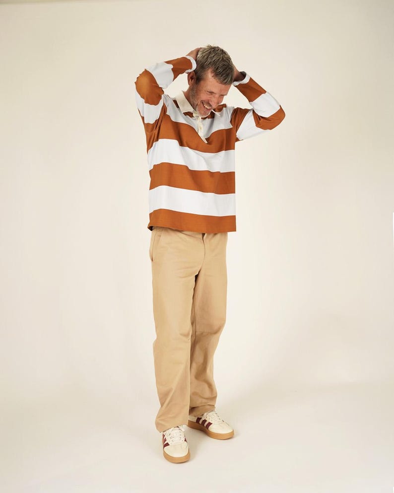 May include: A rugby shirt with horizontal brown and white stripes, paired with khaki pants and white sneakers with burgundy accents. The shirt has a white collar and buttoned placket. The outfit is casual and comfortable.