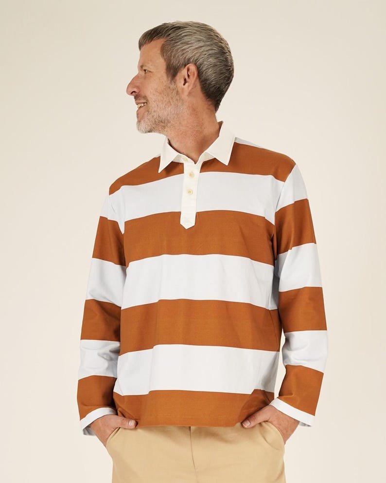 May include: A long-sleeved rugby shirt with horizontal stripes in brown, white, and light blue. The shirt has a white collar and a three-button placket. The person is wearing khaki pants.