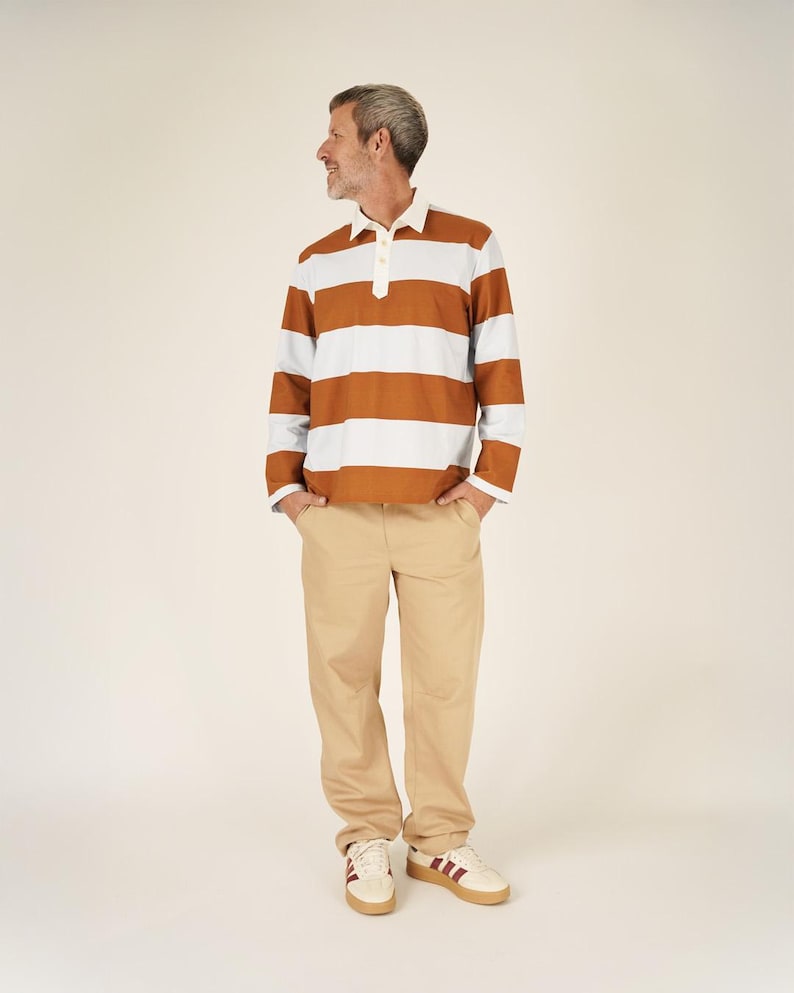 May include: A person wearing a brown and white striped long-sleeve polo shirt, khaki pants, and white sneakers with burgundy stripes. The shirt has a white collar and a three-button placket. The sneakers have a brown sole.