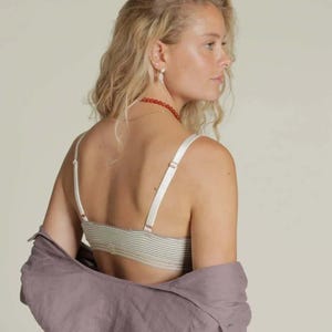 Puede incluir: Un bralette a rayas con tirantes ajustables y una camisa lavanda a juego sobre los hombros. El bralette presenta un patr&oacute;n de rayas verdes claras y blancas. Las correas y los herrajes son de color crema.