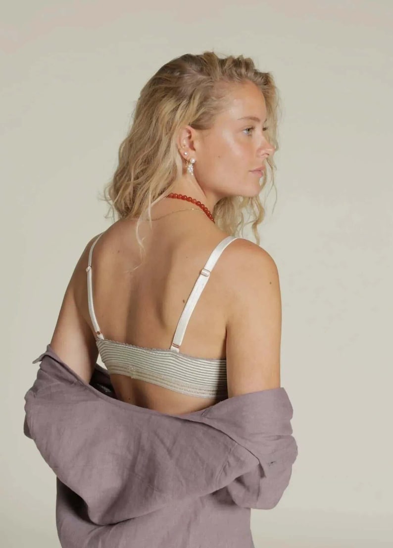 Puede incluir: Un bralette a rayas con tirantes ajustables y una camisa lavanda a juego sobre los hombros. El bralette presenta un patr&oacute;n de rayas verdes claras y blancas. Las correas y los herrajes son de color crema.
