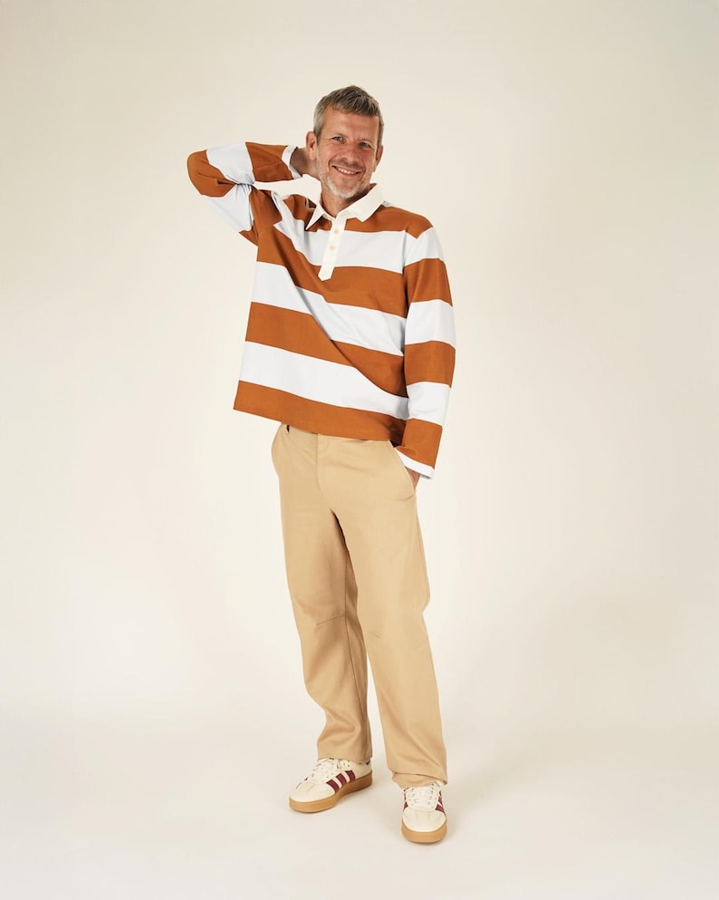 May include: A long-sleeved rugby shirt with horizontal brown and white stripes, paired with khaki pants and cream-colored sneakers with burgundy stripes. The shirt has a white collar and buttoned placket. The outfit is casual and stylish.