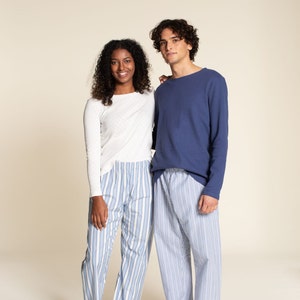 May include: Two people wearing matching pajama sets. One person wears a white long-sleeve shirt with a small dot pattern and blue and white striped pajama pants. The other person wears a navy blue long-sleeve shirt and blue and white striped pajama pants.