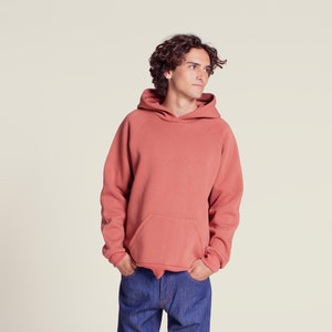 Può includere: Una felpa con cappuccio di colore corallo con una tasca a marsupio. La felpa è realizzata in un tessuto morbido e confortevole.